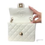 White quilted handbag with gold hardware held by a hand on a white background