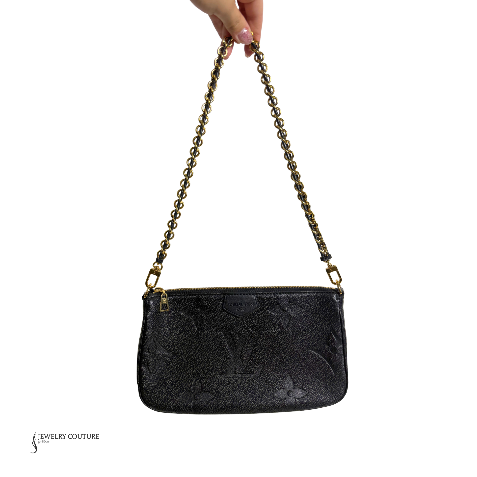 Black handbag with gold chain strap held by a hand on a white background