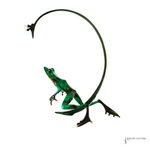 A green frog-shaped jewelry piece with a curved black metal loop arching over it, shown on a plain white background. A small 'Jewelry Couture' logo is visible in the bottom right corner.