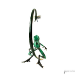 A green frog figurine posed beneath a curved black metal loop, with a small dragonfly above, set against a plain white background.