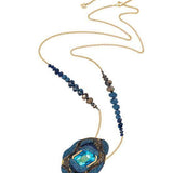 A gold chain necklace featuring a large, textured blue and gold pendant with a central light blue gemstone, accented by rows of dark blue beads on either side of the chain.