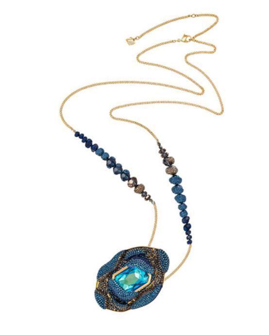 A gold chain necklace featuring a large, textured blue and gold pendant with a central light blue gemstone, accented by rows of dark blue beads on either side of the chain.