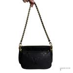 Black handbag with gold chain strap held by a hand on a white background