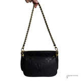 Black handbag with gold chain strap held by a hand on a white background
