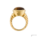 A yellow gold ring featuring a twisted band and a dome-shaped brown tiger's eye stone, shown against a plain white background.