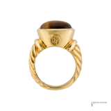 A yellow gold ring featuring a twisted band and a dome-shaped brown tiger's eye stone, shown against a plain white background.
