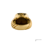 A gold signet ring with a sculpted, ribbed band and a polished oval face, shown from a top-down angle on a white background.