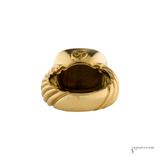 A gold signet ring with a sculpted, ribbed band and a polished oval face, shown from a top-down angle on a white background.