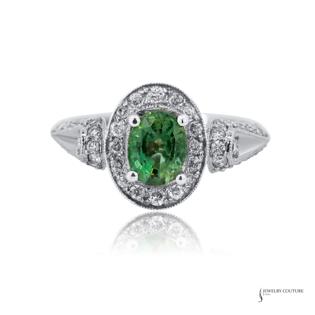 A White Gold Natural Alexandrite & Diamond Halo Ring oval ring featuring a vibrant green oval-cut center stone surrounded by a double halo of small clear stones, with a split shank also accented by diamonds, shown on a white background with a soft reflection.