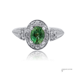 A White Gold Natural Alexandrite & Diamond Halo Ring oval ring featuring a vibrant green oval-cut center stone surrounded by a double halo of small clear stones, with a split shank also accented by diamonds, shown on a white background with a soft reflection.