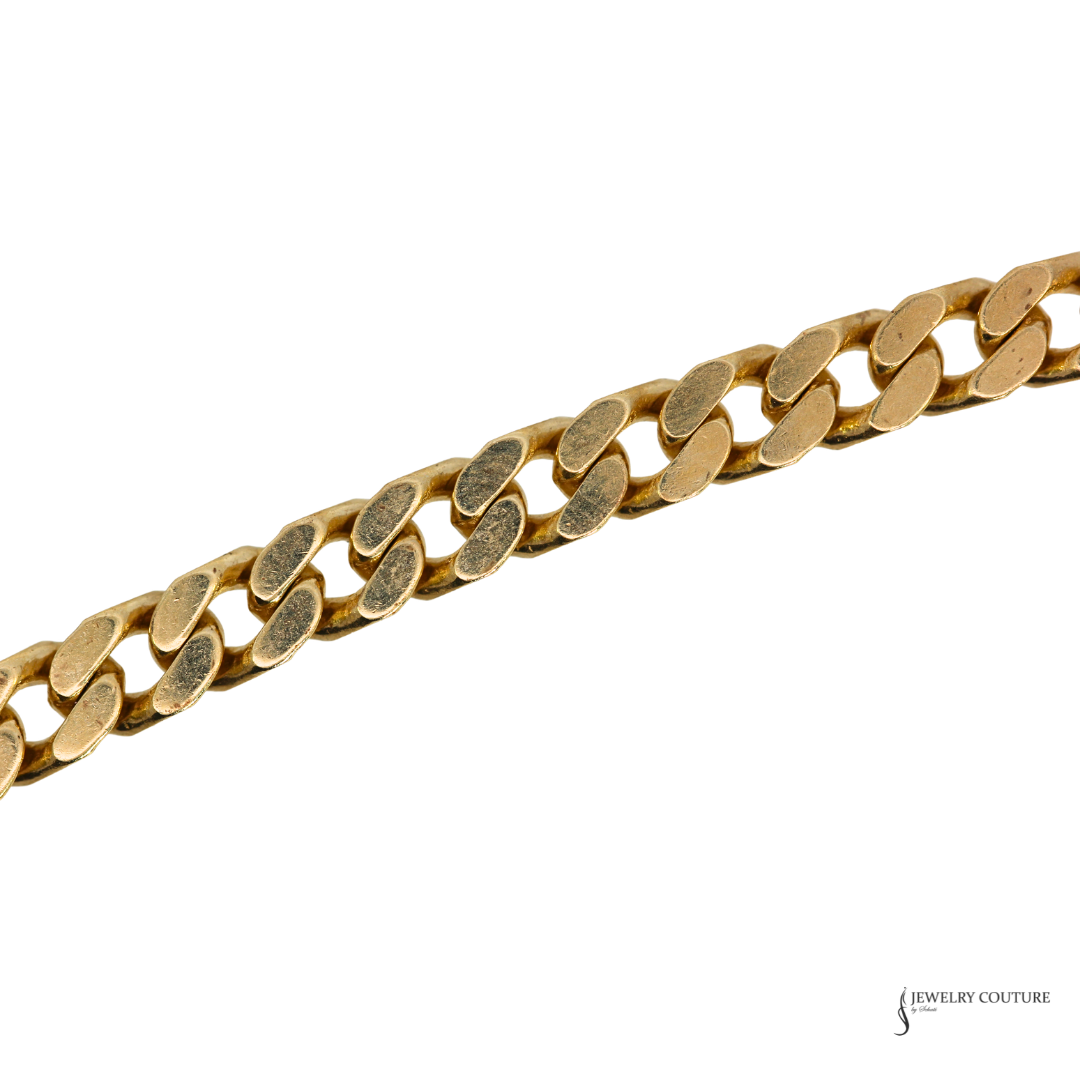 A close-up of a gold Cuban link chain running diagonally across a white background, with a Jewelry Couture logo in the bottom right corner.