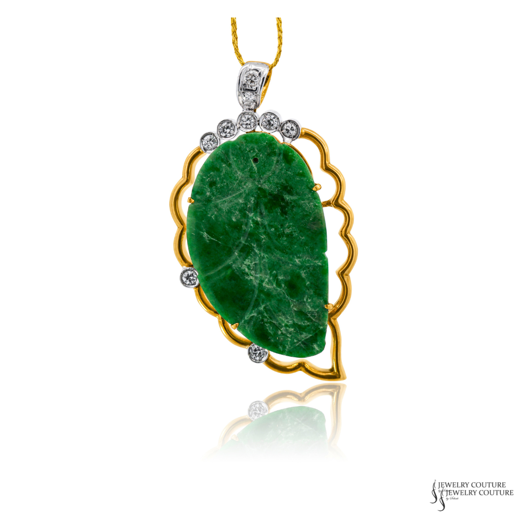 A gold pendant necklace featuring a large, polished green jadeite leaf-shaped cabochon stone, accented with small round-cut diamonds along the top and left scalloped edges, suspended from a gold chain against a white background.