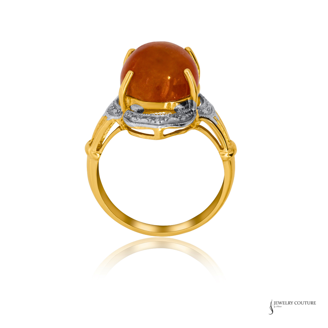 A yellow gold ring featuring a large, polished oval amber cabochon gemstone in a prong setting, accented by a silver-colored band with small clear stones, shown on a white background with a soft reflection.