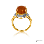 A yellow gold ring featuring a large, polished oval amber cabochon gemstone in a prong setting, accented by a silver-colored band with small clear stones, shown on a white background with a soft reflection.