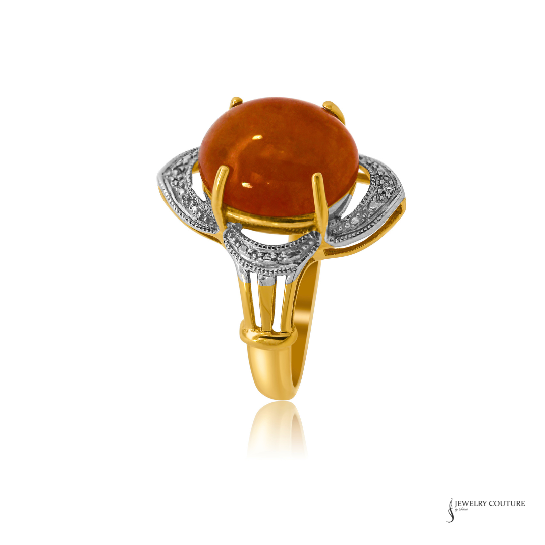 A gold and silver ring featuring a large oval orange cabochon gemstone, with intricate silver filigree details on the shoulders, set against a plain white background.