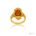 A yellow gold ring featuring a large, irregularly shaped orange-brown gemstone in a decorative setting, shown on a white background with a soft reflection below.