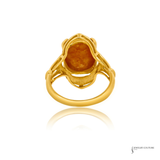A yellow gold ring featuring a large, irregularly shaped orange-brown gemstone in a decorative setting, shown on a white background with a soft reflection below.
