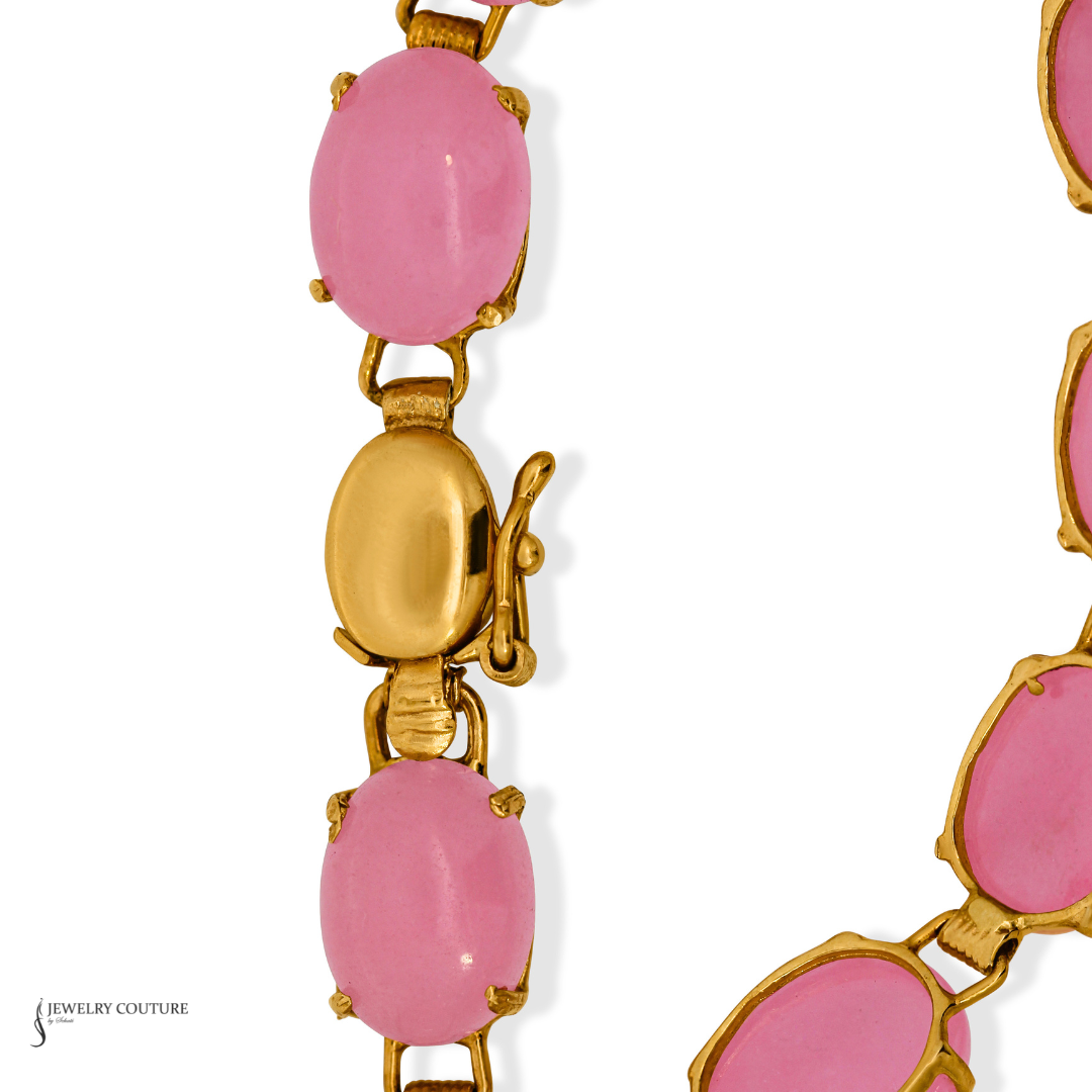 A close-up of a gold-tone chain necklace featuring oval pink cabochon stones, with a lobster clasp visible in the center on a white background.