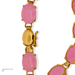 A close-up of a gold-tone chain necklace featuring oval pink cabochon stones, with a lobster clasp visible in the center on a white background.