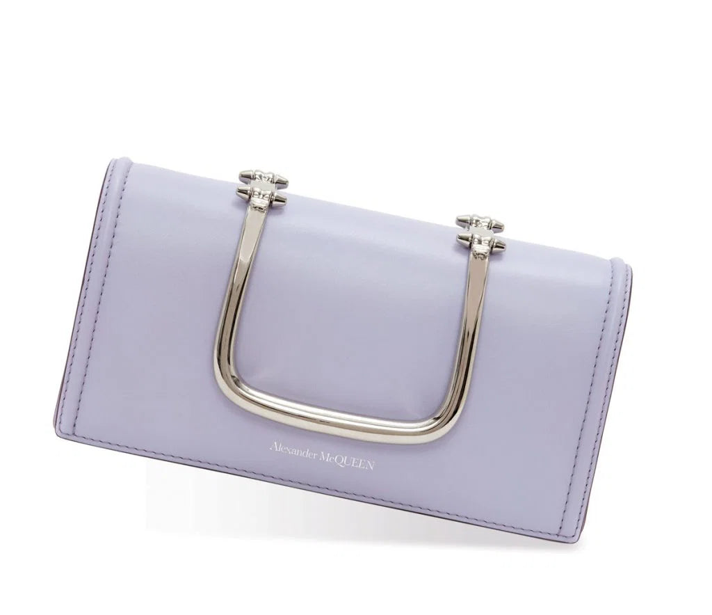 A light purple leather clutch bag with a large silver U-shaped metal handle and silver hardware, featuring the Alexander McQueen logo on the front, set against a plain white background.
