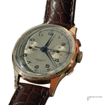 A vintage chronograph wristwatch with a round rose gold-toned case, a silver dial with black Arabic numerals and subdials, and a brown crocodile-embossed leather strap, shown on a white background.