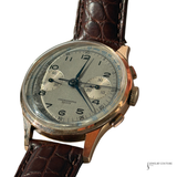 A vintage chronograph wristwatch with a round rose gold-toned case, a silver dial with black Arabic numerals and subdials, and a brown crocodile-embossed leather strap, shown on a white background.