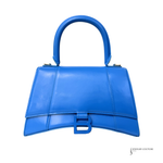 A bright blue leather handbag with a structured top handle and a matching blue B-shaped turn-lock clasp, shown against a plain white background.