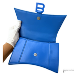 A bright blue leather clutch bag with a matching blue handle, held open by a hand wearing a white glove against a plain white background.