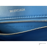 Close-up of a blue textured leather wallet or clutch by Balenciaga, showing the interior zip pocket, gold-tone zipper, and the embossed BALENCIAGA logo on the blue exterior.