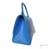 A bright blue leather handbag shown from a side angle against a plain white background, featuring a structured rectangular shape and a top handle.