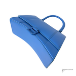 A bright blue structured leather handbag with a top handle and a decorative front clasp, shown on a plain white background.