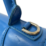 Close-up of a blue leather handbag strap with a gold-tone metal D-ring on a white background.