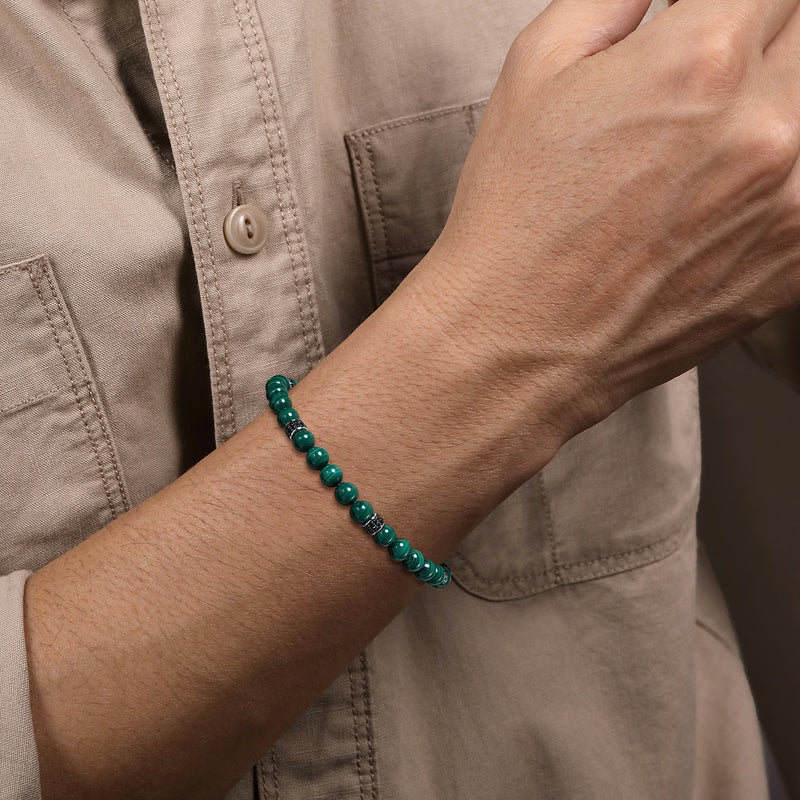 Person wearing a green beaded bracelet on a neutral background