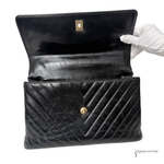 Black quilted handbag with a gold clasp, held open by a gloved hand on a white background.