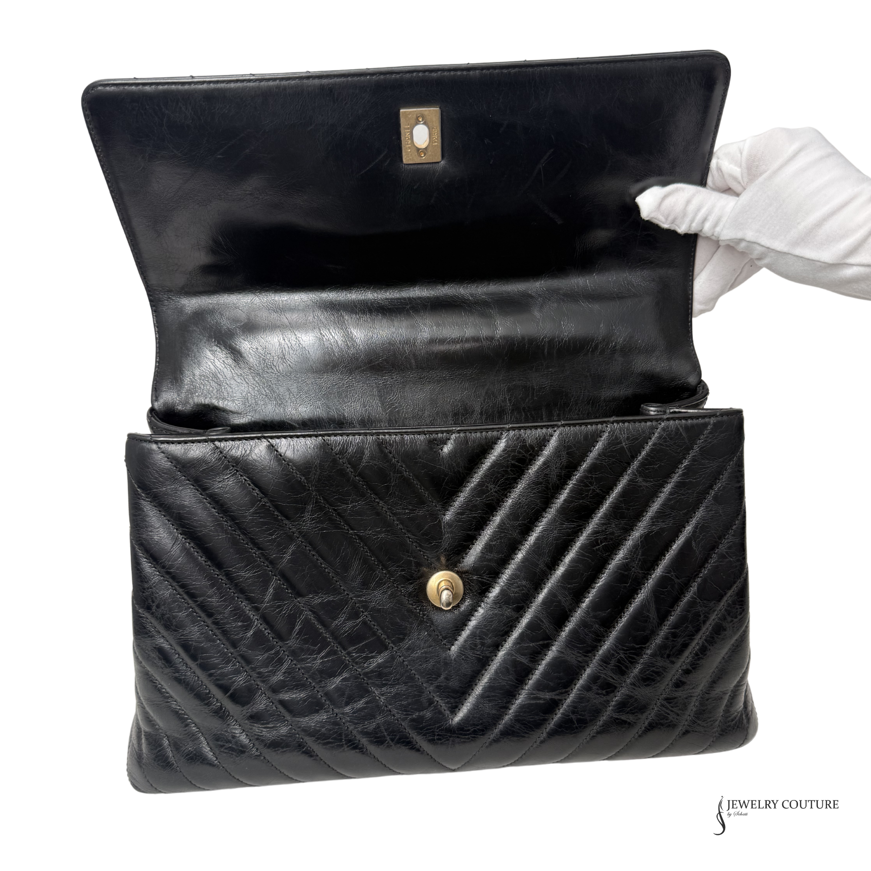 Black quilted handbag with a gold clasp, held open by a gloved hand on a white background.