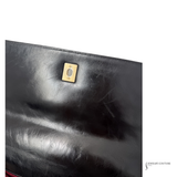 Close-up of a black leather clutch with a gold clasp on a white background.