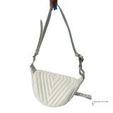 White quilted crossbody bag held by a hand on a white background