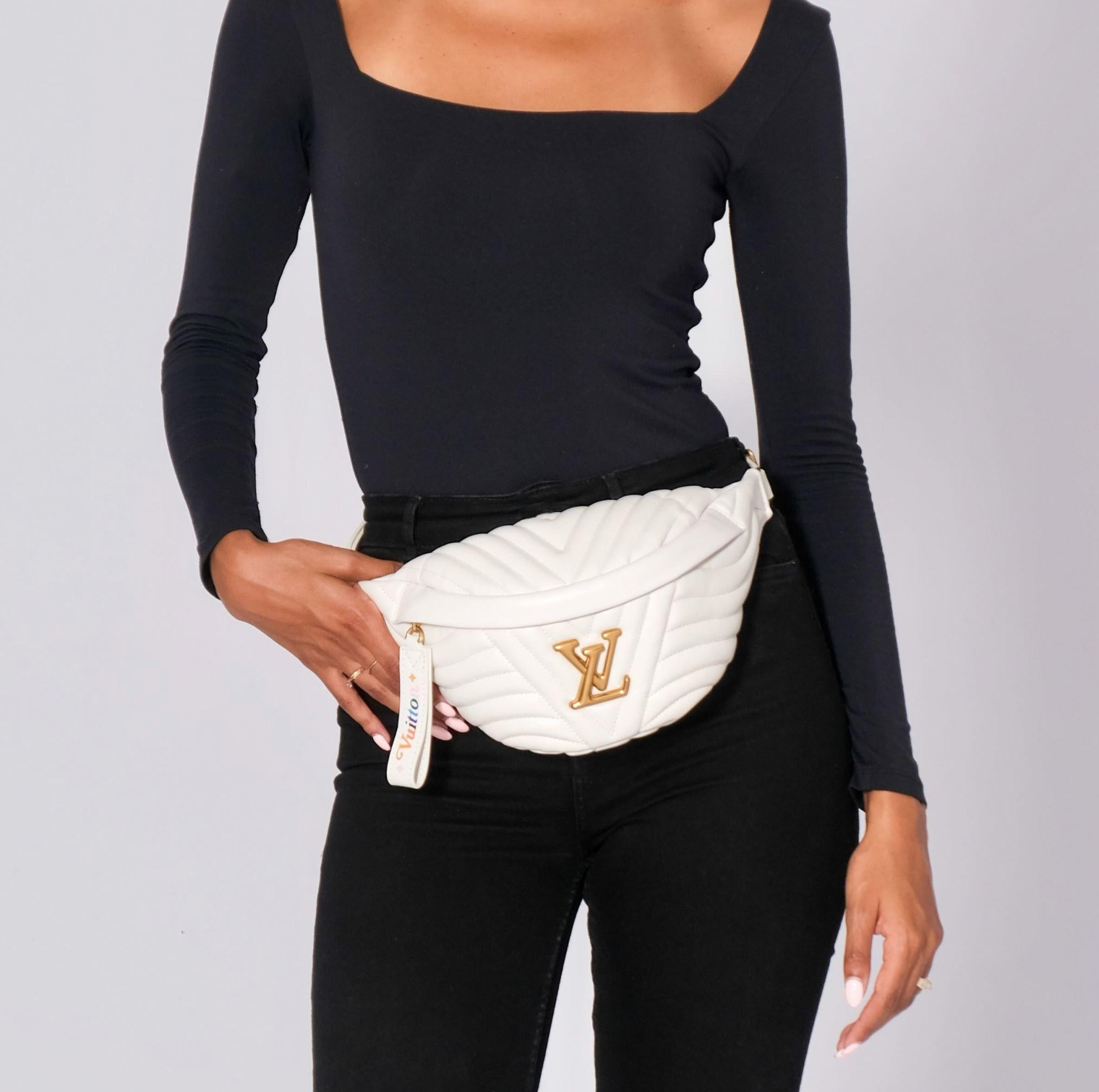 Person wearing a white quilted fanny pack with a brand logo on a plain background