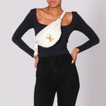 Person wearing a black long-sleeve top and black pants with a white fanny pack on a light gray background