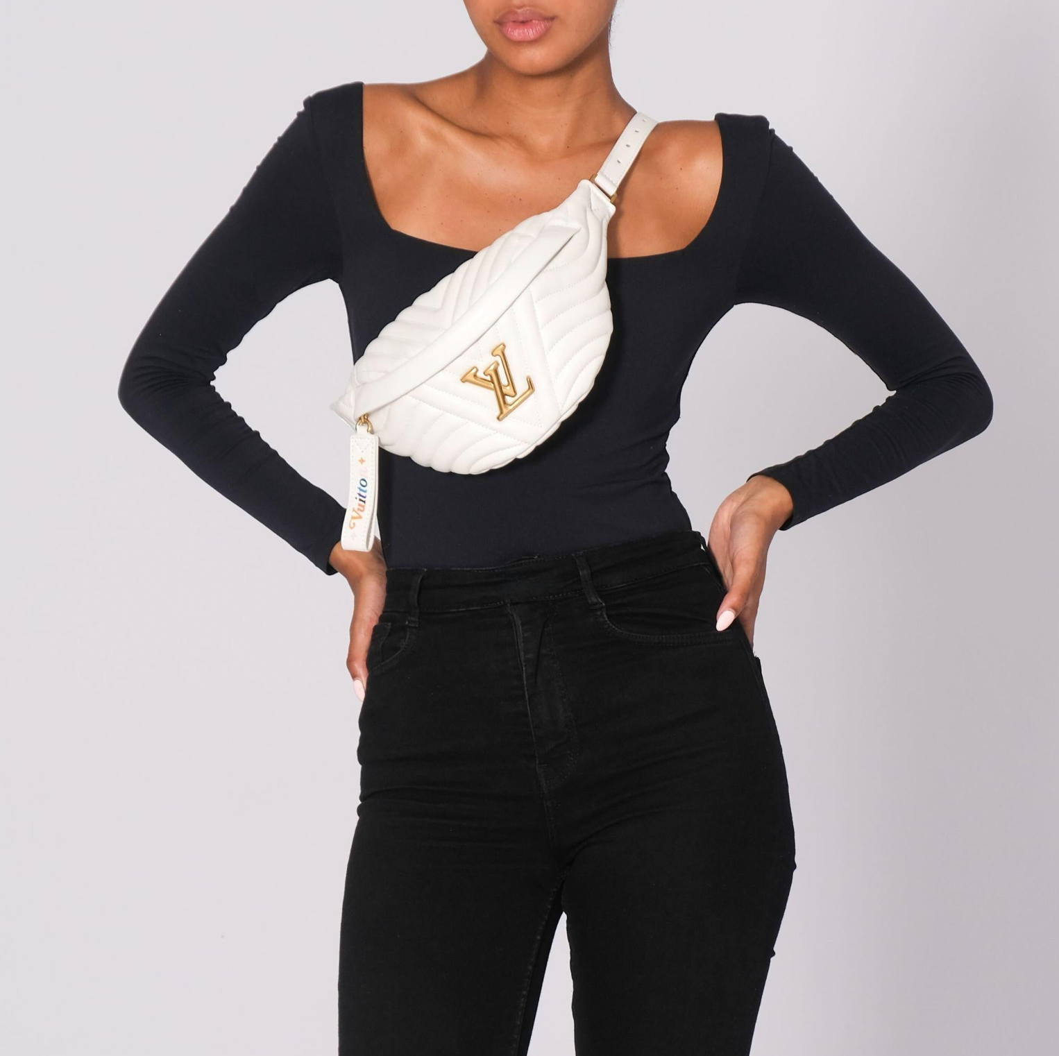 Person wearing a black long-sleeve top and black pants with a white fanny pack on a light gray background