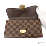 Brown checkered handbag with gold accents held by a gloved hand on a white background