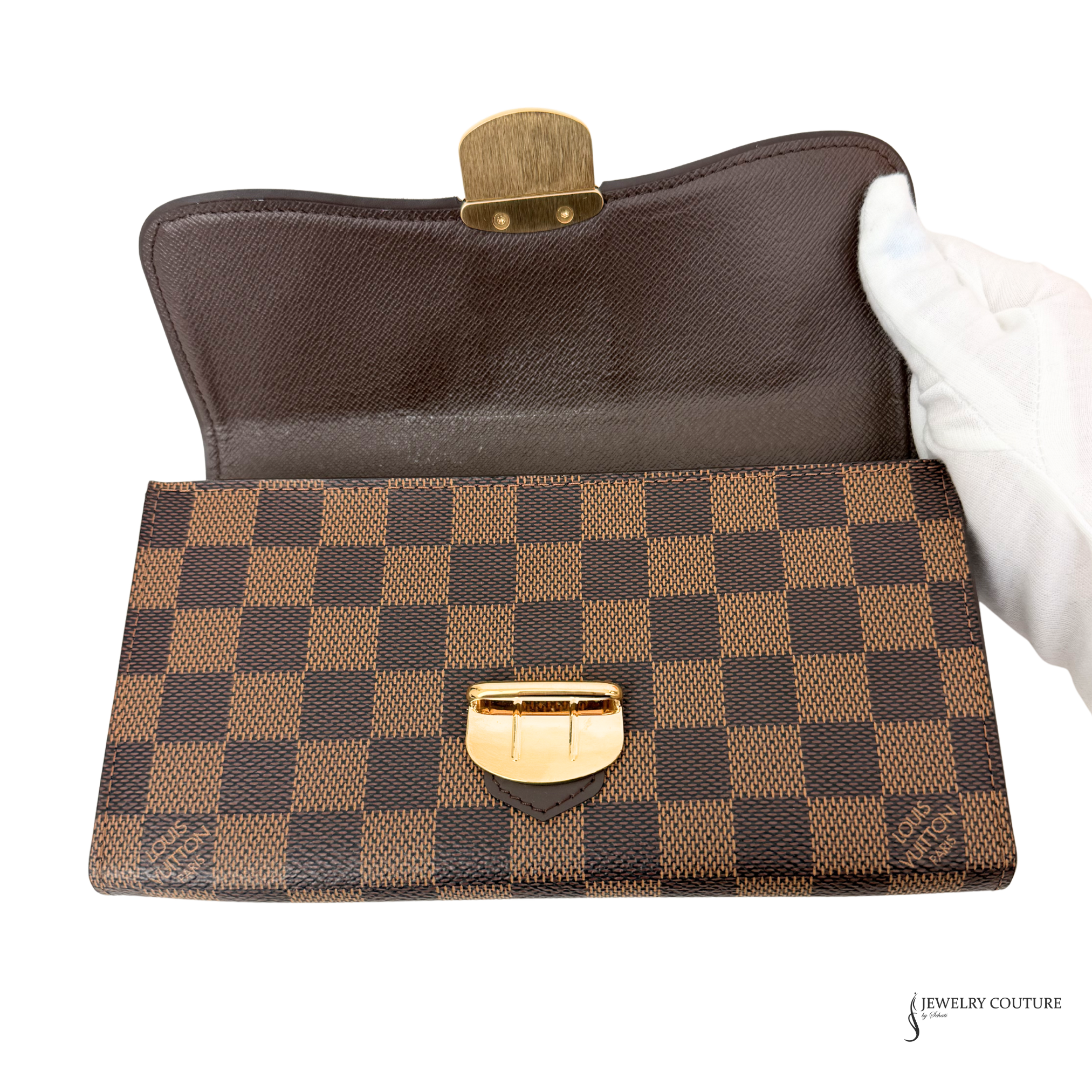 Brown checkered handbag with gold accents held by a gloved hand on a white background