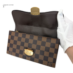 Brown checkered clutch bag with gold clasp held by a gloved hand on a white background