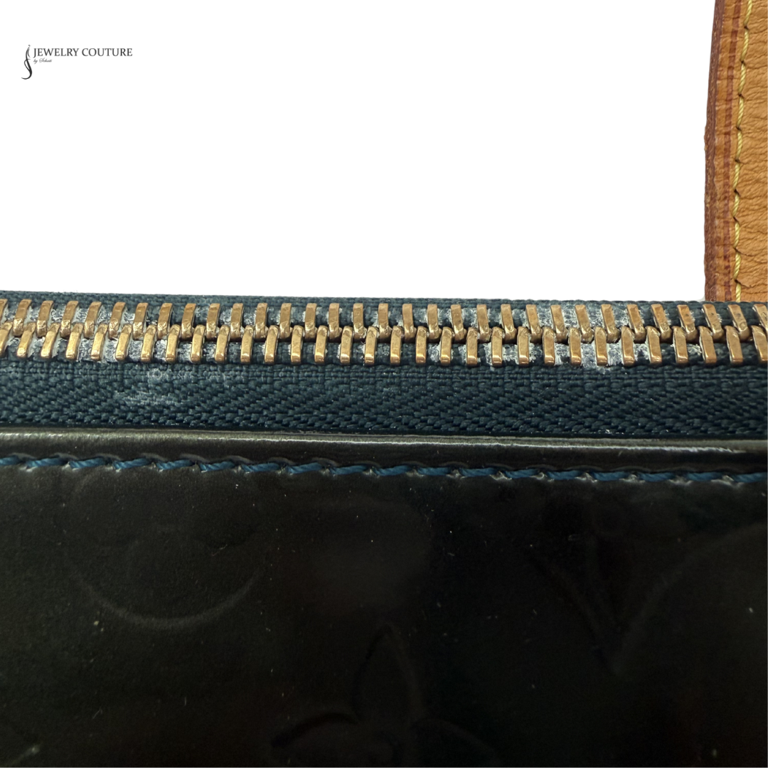 Close-up of a black handbag with gold zipper and brown handle.