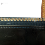 Close-up of a black handbag with gold zipper and brown handle.