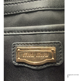 Close-up of a black leather product with a gold Miu Miu label.