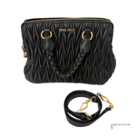 Black textured handbag with gold accents and matching strap on a white background