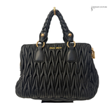 Black quilted handbag with braided handle on a white background