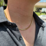 A close-up of a person's neck and chest wearing a gold chain necklace over a dark gray patterned button-up shirt.