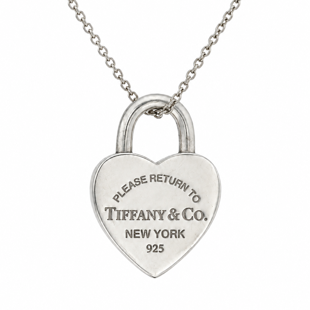 A silver heart-shaped padlock pendant necklace engraved with 'PLEASE RETURN TO TIFFANY & Co. NEW YORK 925', suspended from a delicate silver chain against a plain white background.